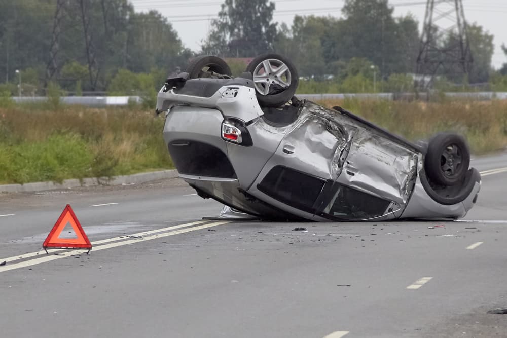 Overturned car on a highway after a serious accident, with visible damage to the roof and front end.