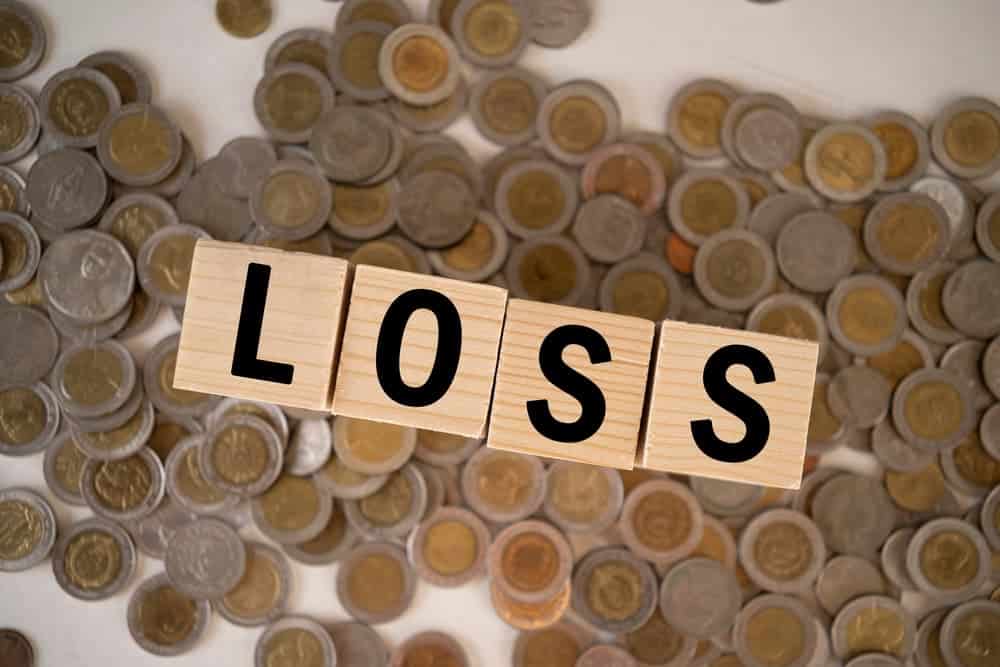 Wooden blocks spelling “LOSS” placed on top of stacked coins, symbolizing financial loss or economic downturn.