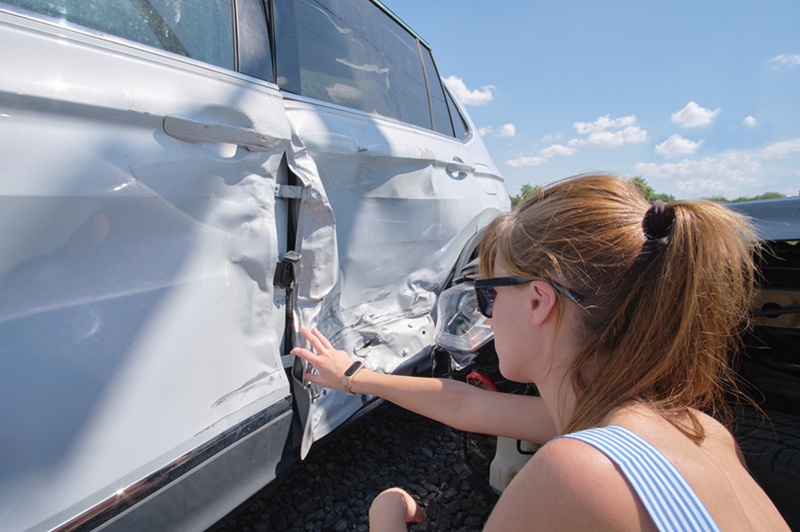 Sad female driver sitting on street side shocked after car accident. Road safety and vehicle insurance concept.