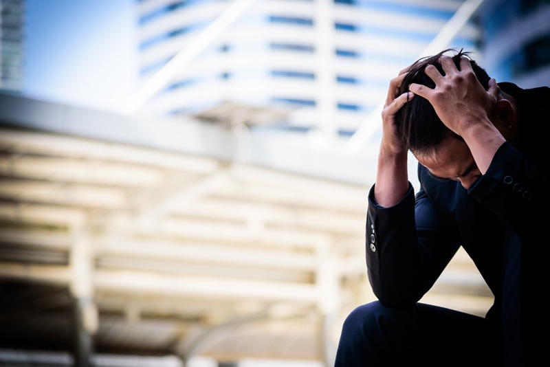 Man sits on a bench in the city, holding his head in frustration and confustion